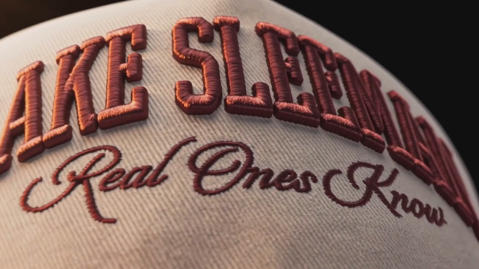 Macro detail of raised maroon embroidery on a cream cap